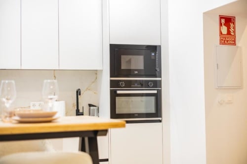 Cocina moderna en apartamento de Cuenca con muebles blancos, horno y microondas empotrados negros, backsplash de mármol, mesa de comedor,