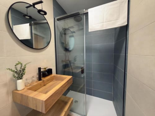 Baño moderno en apartamento de Cuenca con lavabo de madera, espejo marco negro, ducha de cristal y paredes de azulejos oscuros