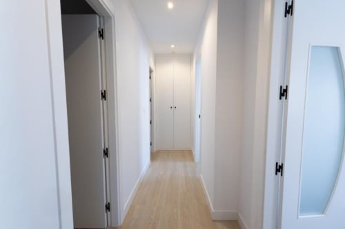 Pasillo moderno con puertas blancas y pisos de madera en apartamento de Cuenca, acceso a armarios del dormitorio