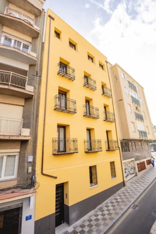Luminoso edificio amarillo en Cuenca, España con balcones de hierro y múltiples ventanas en una calle estrecha.