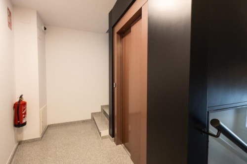 Pasillo del edificio con puertas de madera, extintor de incendios y escalera en Apartamentos La Búsqueda, Cuenca