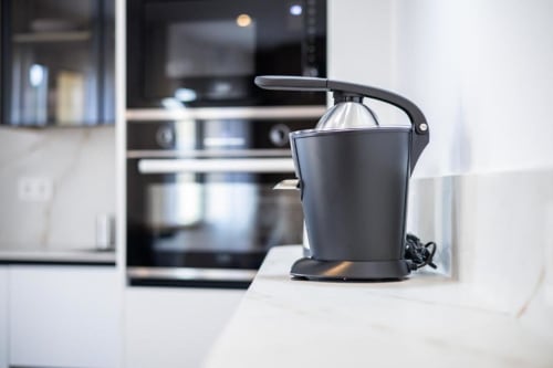 Exprimidor de cítricos negro en la encimera blanca de la cocina del apartamento en Cuenca con horno empotrado visible