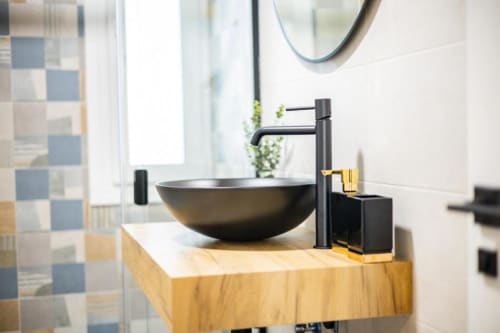 Lavabo negro moderno con grifo mate sobre tocador de madera en baño de apartamento en Cuenca con pared de azulejos a cuadros