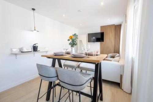 Comedor moderno en apartamento de 2 dormitorios en Cuenca con mesa de madera, sillas grises y vista a la ciudad desde el balcón