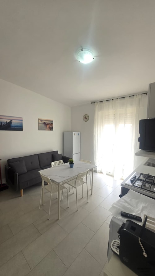 Luminosa cucina-soggiorno moderna con vista mare in appartamento a Tronca, Italia. Cucina a gas, tavolo da pranzo, divano e luce naturale