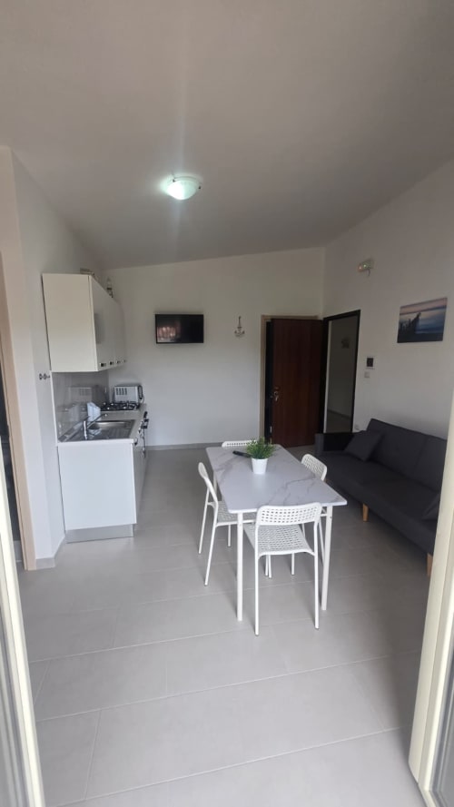 Cucina e zona living moderne con arredamento bianco, angolo cottura attrezzato e divano nero, affaccio sulla spiaggia di Tronca
