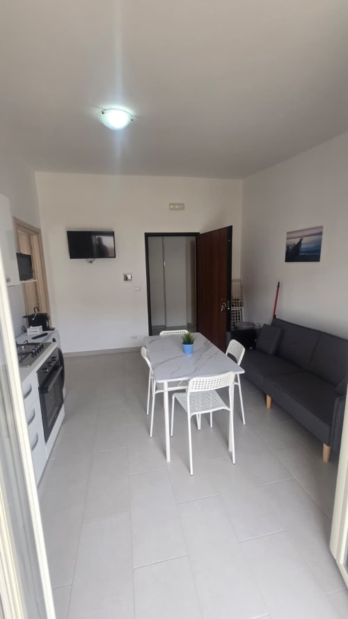Moderno appartamento open-plan a Tronca con tavolo da pranzo, cucina, divano nero e TV a schermo piatto vicino alla spiaggia