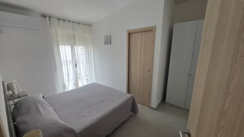Camera luminosa con letto grigio, armadio in legno, porte-finestre verso balcone, appartamento con vista mare a Tronca vicino alla spiaggia