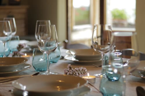 Mesa elegante en Casa Tapiolas con copas de vino, cubiertos y flores frescas con vistas a los jardines de Molló