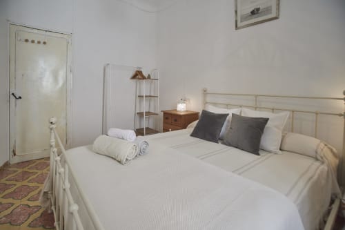 Habitación luminosa en villa Casas Cercana de Abarán con cama de hierro color crema, ropa blanca, almohadas oscuras, mesita de noche de madera