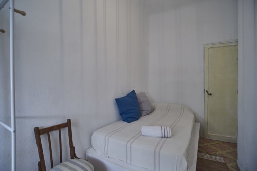 Dormitorio sencillo con paredes blancas, cama individual con almohada azul, silla de madera y puerta color crema en la villa Casas Cercana en Abarán