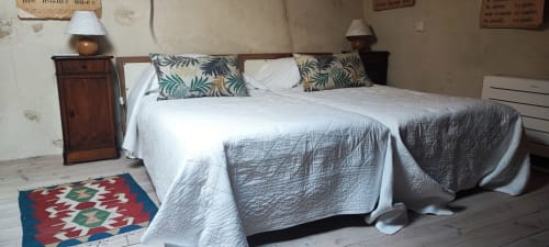 Chambre chaleureuse du gîte Magnanerie de Sainte Croix avec literie matelassée, coussins décorés, table de nuit en bois et tapis coloré