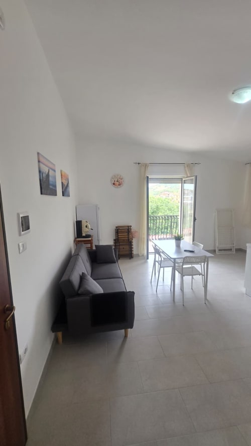 Luminoso soggiorno con vista mare, divano nero, tavolo da pranzo e accesso al balcone presso Tramontana Casa vacanza a Tronca