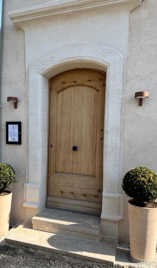 Porte voûtée en bois à l'entrée de La Maison des Jardins B&B à Gigondas, façade en pierre claire et topiaires.