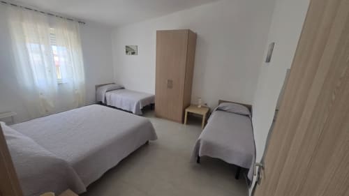 Camera da letto dell'appartamento Tramontana con tre letti singoli, armadio in legno e finestra con vista sul mare a Tronca, Italia