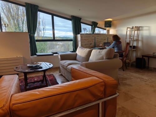 Spacieux salon d'un appartement pour 2 personnes avec vue sur jardin, canapé crème, sièges en cuir, bureau de travail et grandes fenêtres à la Magnanerie