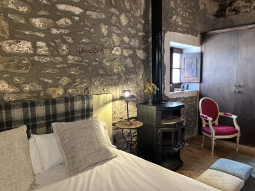Dormitorio de Casa Tapiolas en Molló con muros de piedra rústica, cama confortable, chimenea oscura y muebles de época