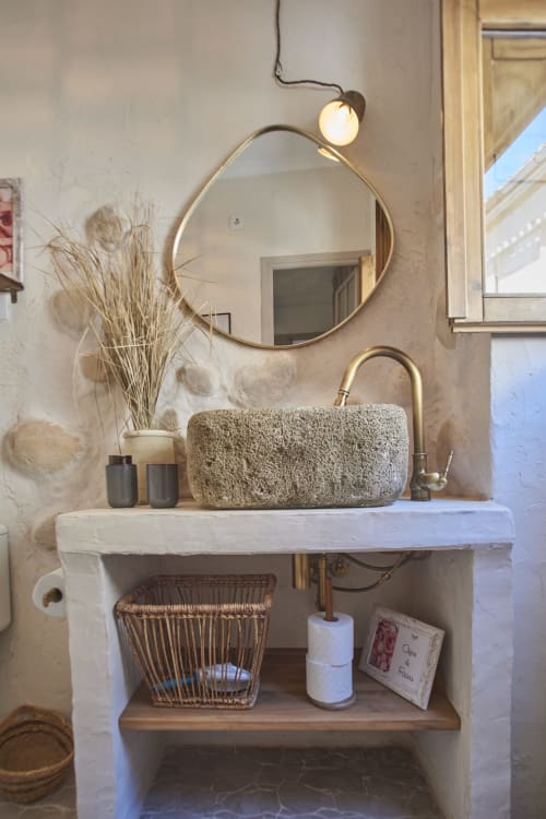 Lavabo rústico del hotel Casas Cercana en Abarán con pileta de piedra, espejo redondo de latón y accesorios decorativos
