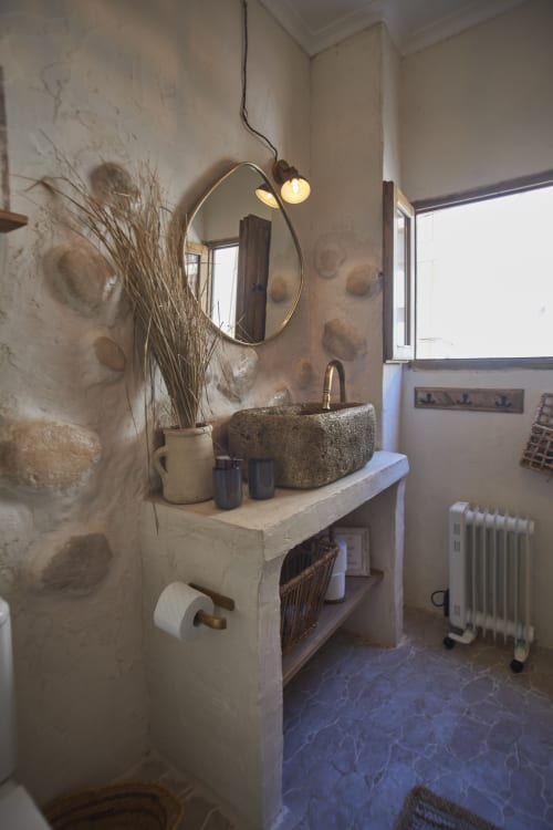 Baño rústico con espejo redondo, lavabo de piedra y decoración de pared texturizada en el hotel Casas Cercana de Abarán