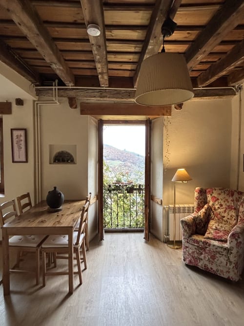 Habitación de Casa Tapiolas en Molló con vigas de madera vista, mobiliario rústico y vistas a las montañas desde el balcón privado