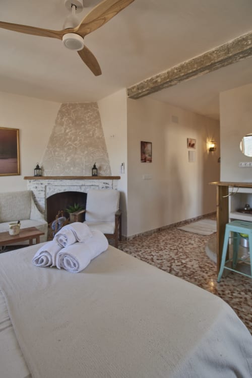 Amplio dormitorio loft en Abarán con chimenea, ventilador de madera, ropa de cama blanca y vigas rústicas