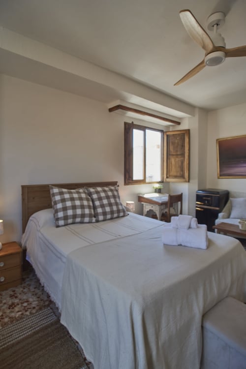 Dormitorio luminoso en Casas Cercana de Abarán con cama de madera, almohadas cuadriculadas, ventilador de techo y vistas a las montañas
