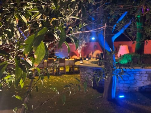 Vue nocturne du Riad Eucalyptus avec éclairage bleu et rose, terrasse aménagée et verdure luxuriante à El Ghazouane, Maroc