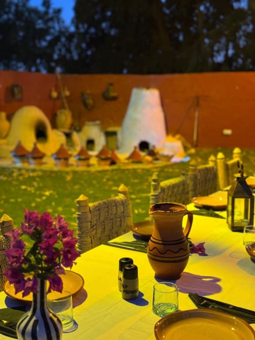 Table à diner du Riad Eucalyptus avec linge jaune, fleurs magenta, poterie traditionnelle et lanternes au crépuscule