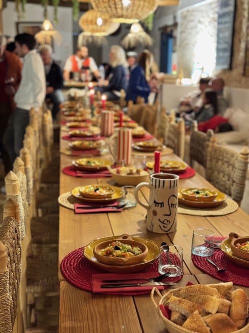 Table à manger rustique au Riad Eucalyptus avec sets de table rouges, bols à tajine et corbeilles de pain