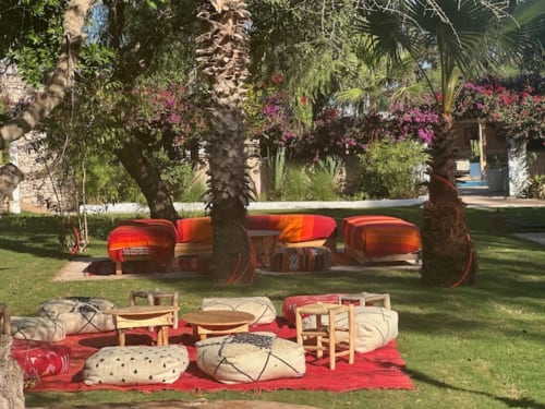 Cour du Riad Eucalyptus avec poufs rouges et sièges bas sous les palmiers, El Ghazouane Maroc