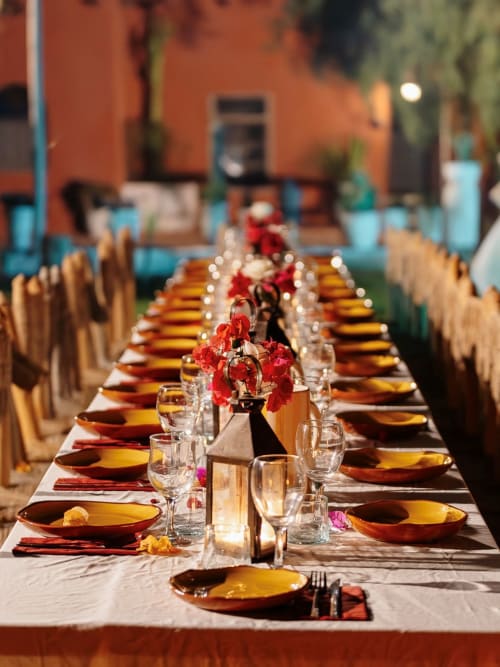 Table de salle à manger élégante au Riad Eucalyptus avec assiettes jaunes, fleurs rouges et architecture marocaine rustique.