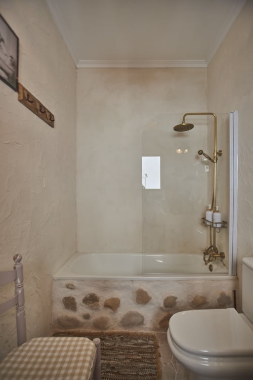 Baño moderno de casa rural con ducha a ras de suelo, herrajes en bronce y detalles en piedra de río en Casas Cercana, Abarán