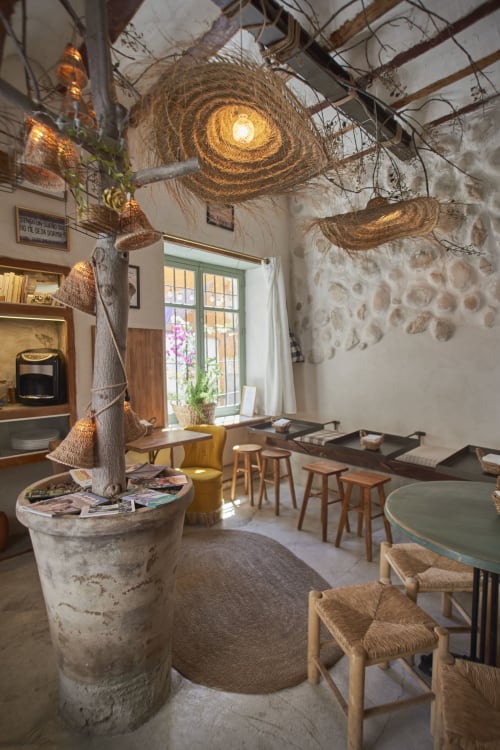 Sala de estar rústica con luces colgantes de cuerda, vigas de madera, asientos cómodos y luz natural en Casas