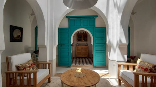 Riad Dar Kleta lounge in Marrakech with turquoise doors, arched ceilings, wooden chairs, and round table