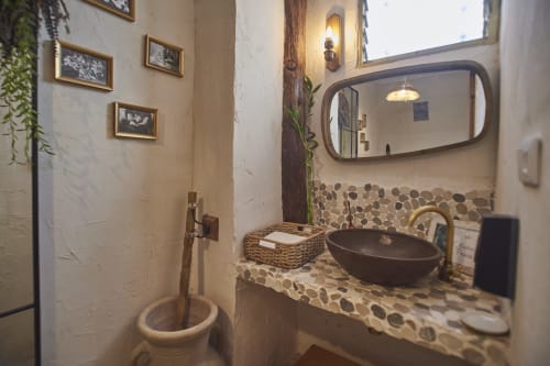 Baño rústico con lavamanos redondo oscuro, espejo circular, revestimiento de guijarros y detalles de madera en la cabaña Casa Cercana, Abarán