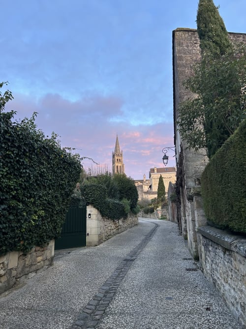 Charming cobblestone street in Saint-Emilion with church spire, ivy-covered stone walls, and historic architecture at dusk
