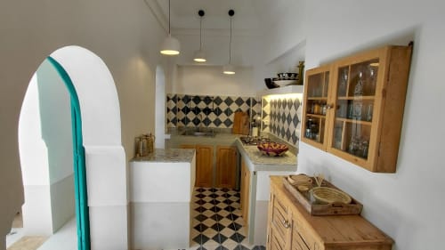 Modern kitchen in Marrakech riad with black and white diamond tile backsplash, wooden cabinetry, and arched turquoise doorway
