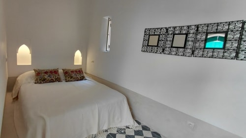 Minimalist bedroom at Riad Dar Kleta in Marrakech with white bed, arched alcove lighting, and decorative wall art