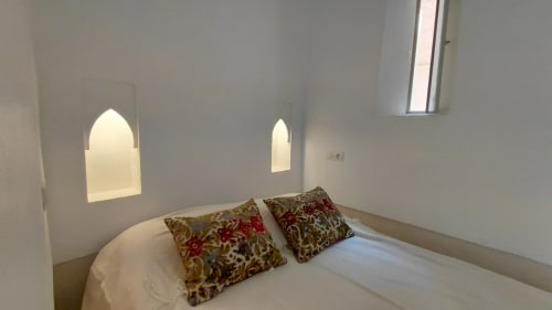 Minimalist bedroom at Riad Dar Kleta in Marrakech with white bed, patterned pillows, and arched alcoves with warm lighting