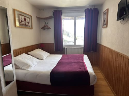 Chambre double de l'Hôtel la Source avec vue montagne, lambris, rideaux violets et TV à La Foux