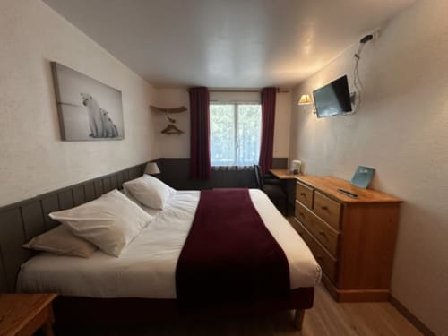 Chambre double de l'Hôtel la Source avec lit queen-size, bureau en bois, TV et rideaux bordeaux à La Foux