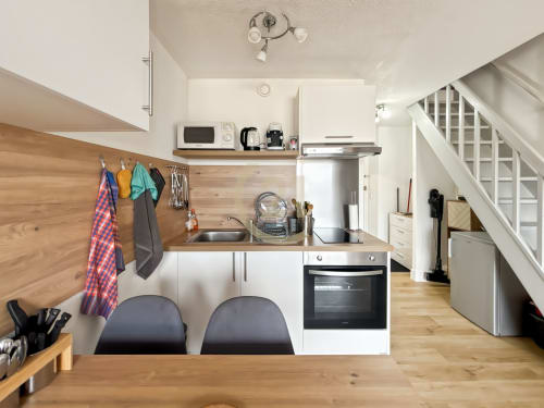 Cuisine moderne de l'appartement L'Île-Rousse près de la plage de Calvi avec meubles blancs, plan de travail en bois et accès par escalier.