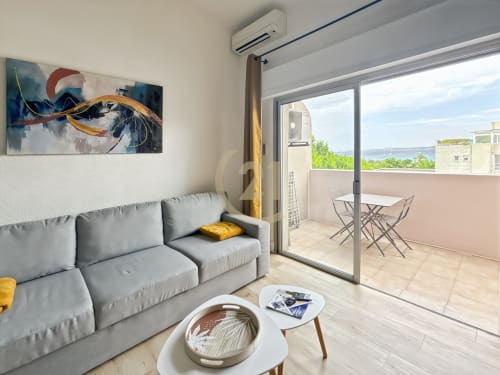 Studio contemporain à L'Île-Rousse avec balcon vue mer, canapé gris et paysage côtier visible par baies vitrées