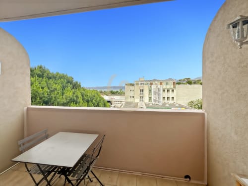 Balcon du studio duplex avec vue sur L'Île-Rousse et la mer, table et chaises, montagnes en arrière-plan
