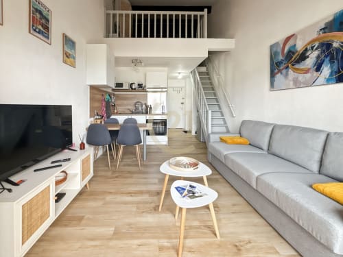 Studio duplex à L'Île-Rousse avec séjour, cuisine, canapé gris, TV et escalier vers la mezzanine