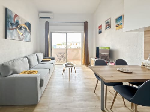 Lumineux studio à L'Île-Rousse : canapé gris, table à manger en bois, TV, balcon vue mer, mobilier moderne