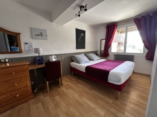Spacieuse chambre double de l'Hôtel la Source, La Foux, avec lit bordeaux, bureau en bois et grandes fenêtres