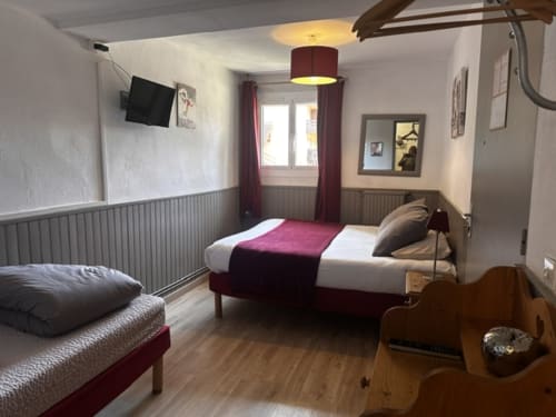 Chambre triple à l'Hôtel la Source à La Foux avec deux lits, accents bordeaux, parquet et équipements modernes