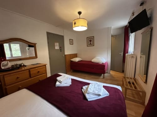Chambre triple à l'Hôtel la Source avec lits bordeaux, meubles en bois et parquets à La Foux.