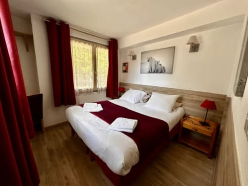 Spacieuse chambre quadruple à l'Hôtel la Source avec lit queen-size, accents bordeaux, mobilier en bois et vue sur les montagnes